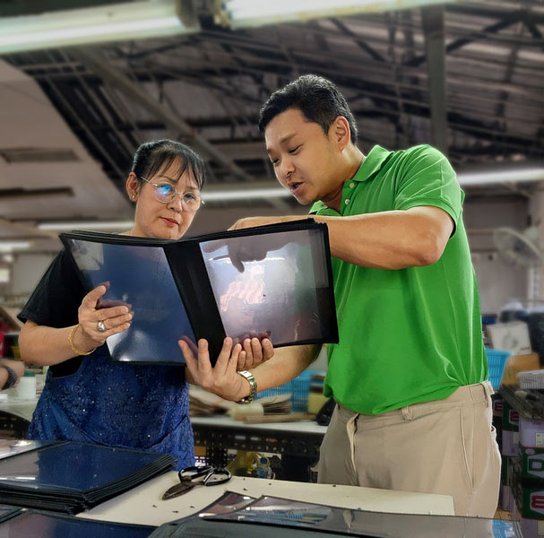 Two coworkers in a workshop review a binder with photos together