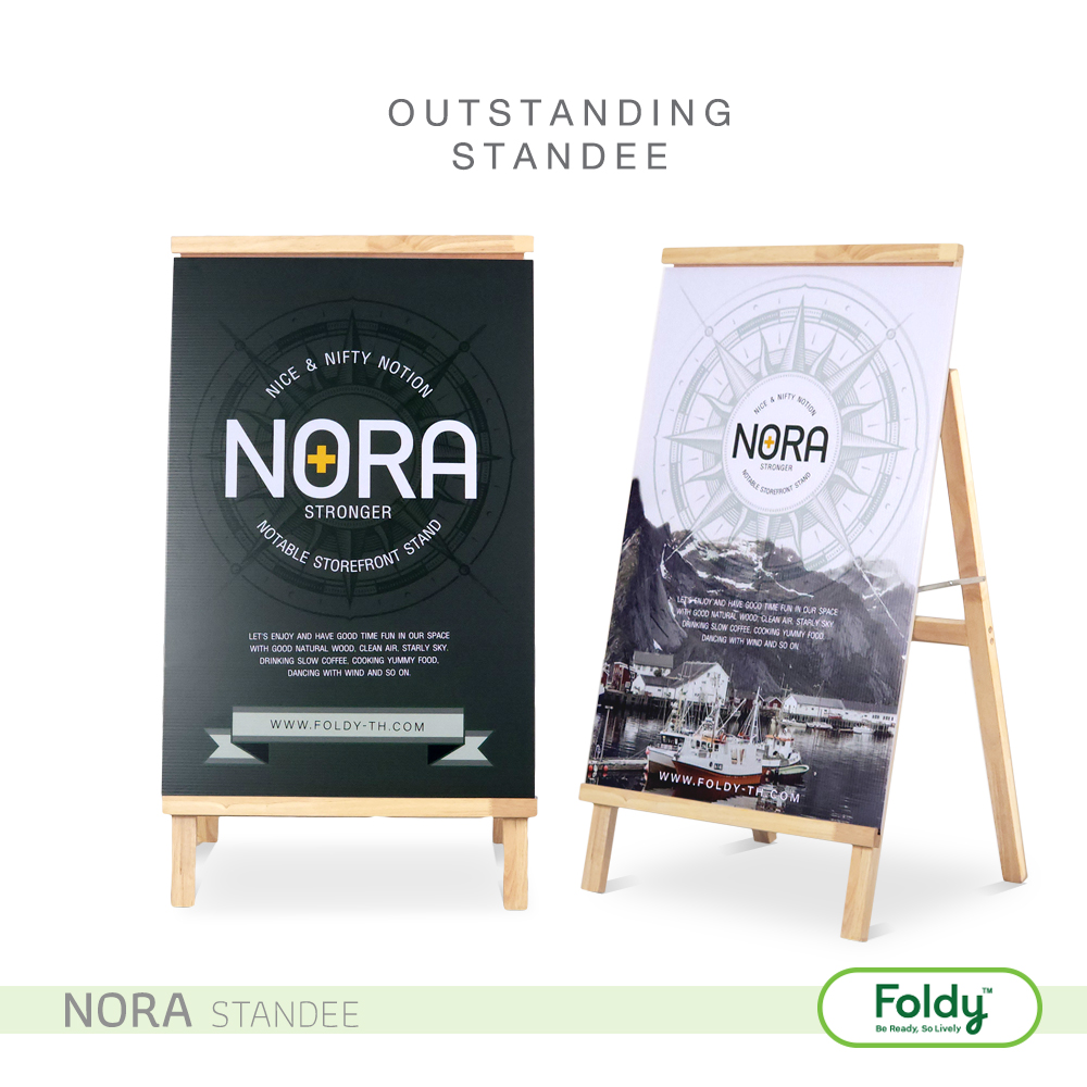 Two Nora standee promotional boards on wooden frames, one dark with NORA logo and 'STRONGER', the other lighter with compass design and mountain scene, side by side.