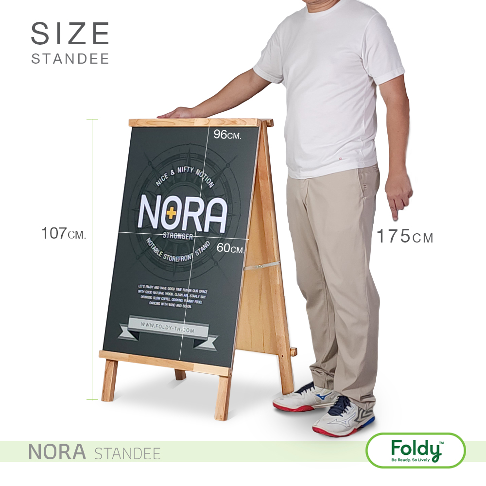 Man in a white t-shirt and beige pants stands beside a chalkboard A-frame sign showing Nora Standee branding and dimensions (107 cm tall, 96 cm wide, 60 cm base).