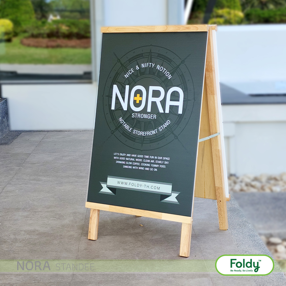 Outdoor wooden A-frame chalkboard sign advertising the NORA storefront stand, with Foldy logo in the lower right corner.”, “Sidewalk promotional sign featuring a circular NORA design and brand text on a dark board with a wooden frame.”, “Public display board for Nora storefront stand, showing the NORA logo and supporting text.”, “Promotional sidewalk board for Nora, with Foldy logo and a green-trostained banner at the bottom.”